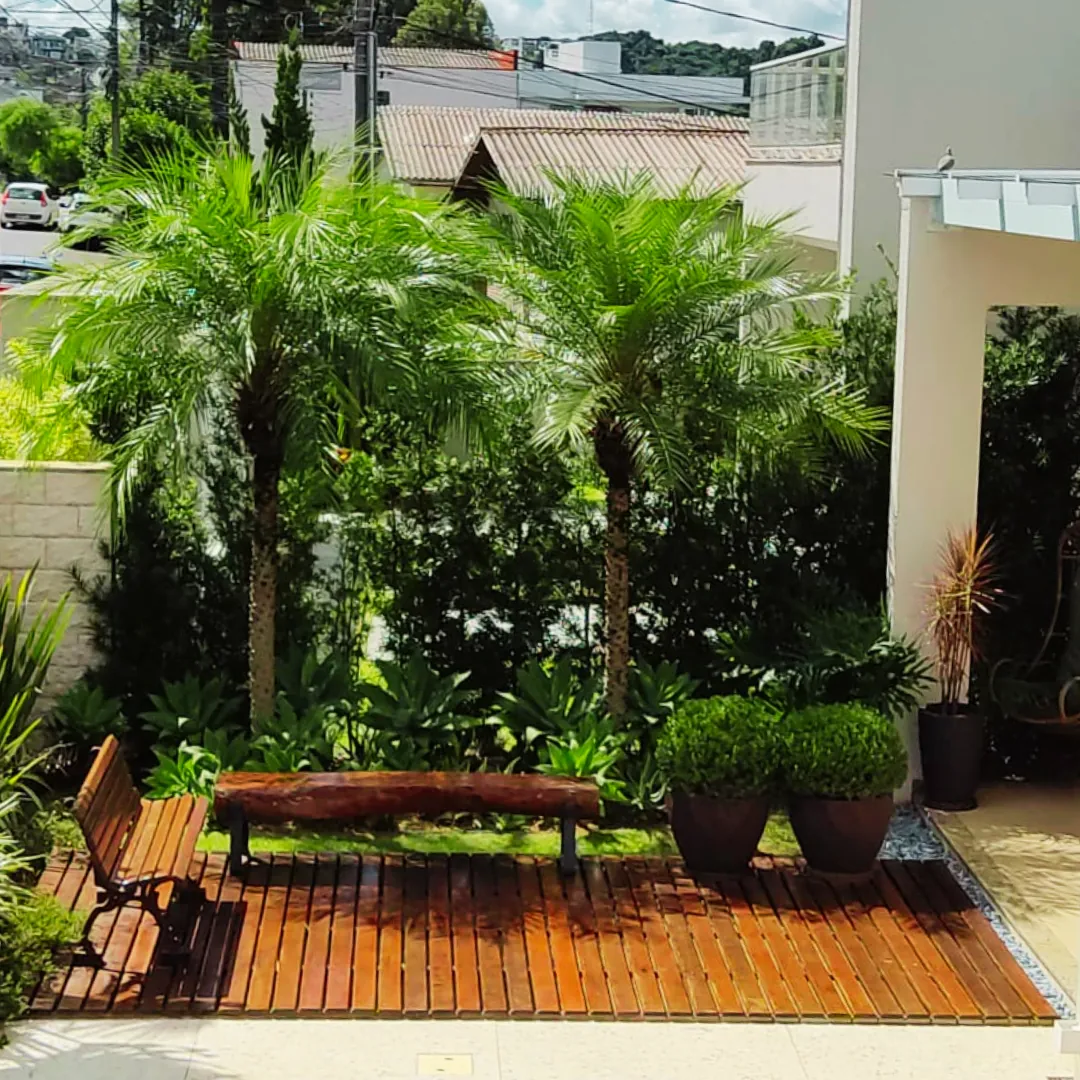 Jardim com palmeiras, deck de madeira e banco feito pela Fredy Rempel Paisagismo em Pato Branco